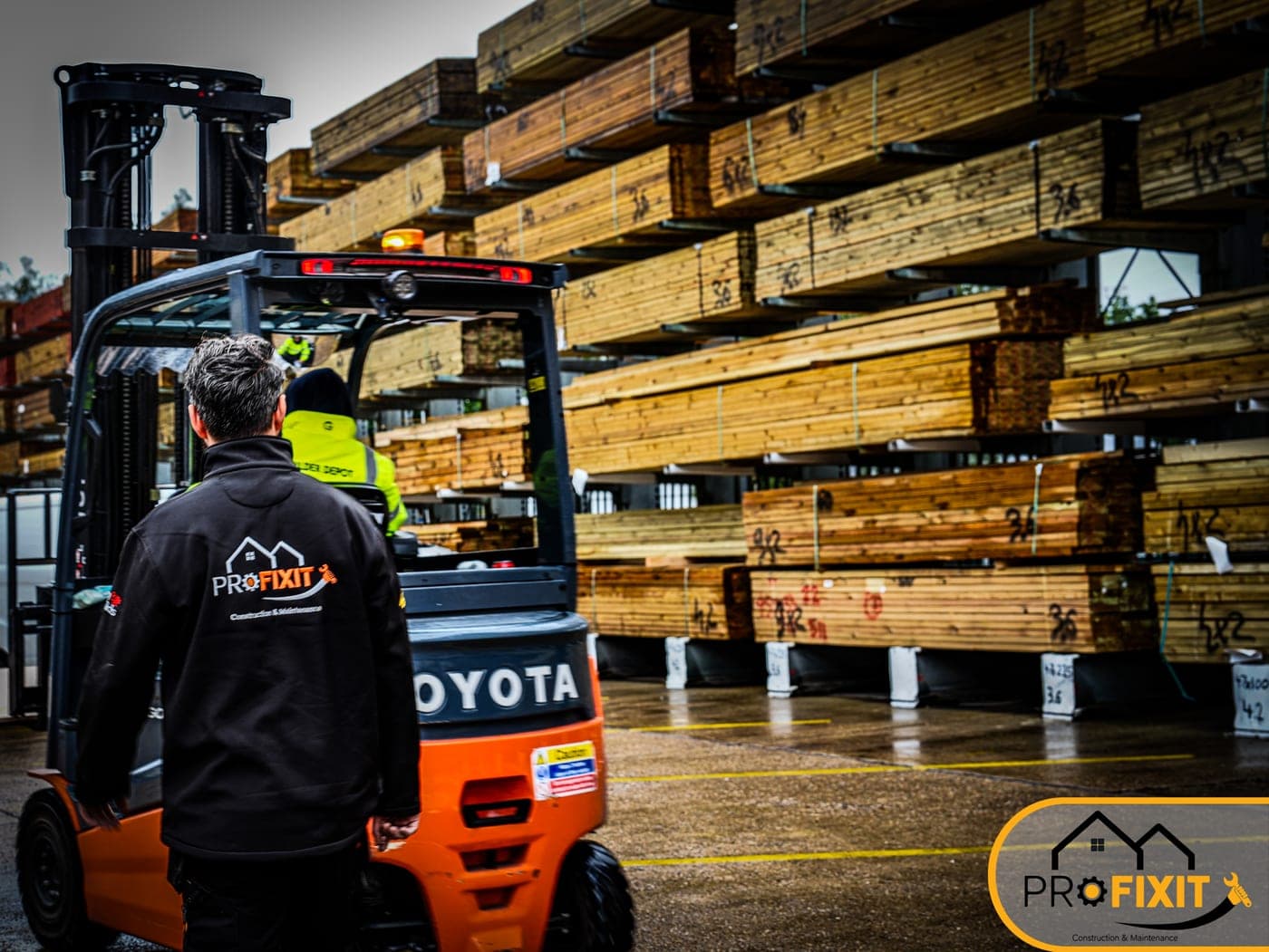 A Pro Fixit worker standing near a forklift and stacked timber.
