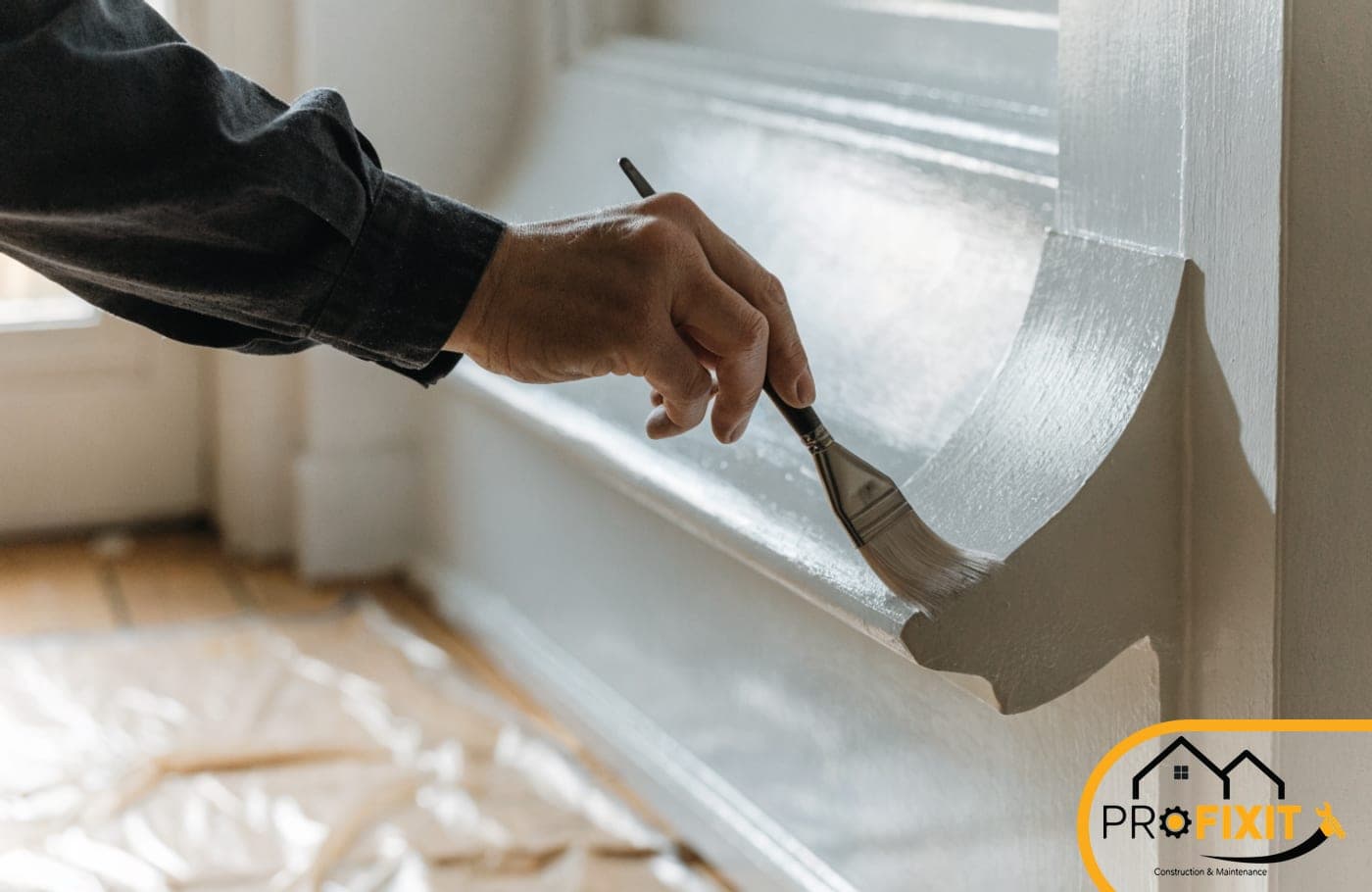 A hand cutting in a paint edge along window architrave with an angled brush, dust sheet below.