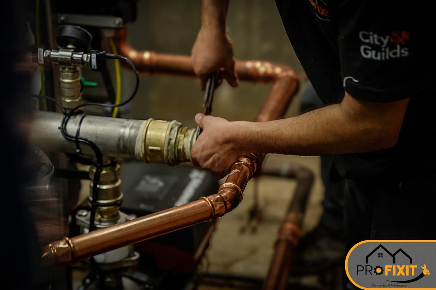 A worker in black workwear fitting copper pipework and brass fittings.