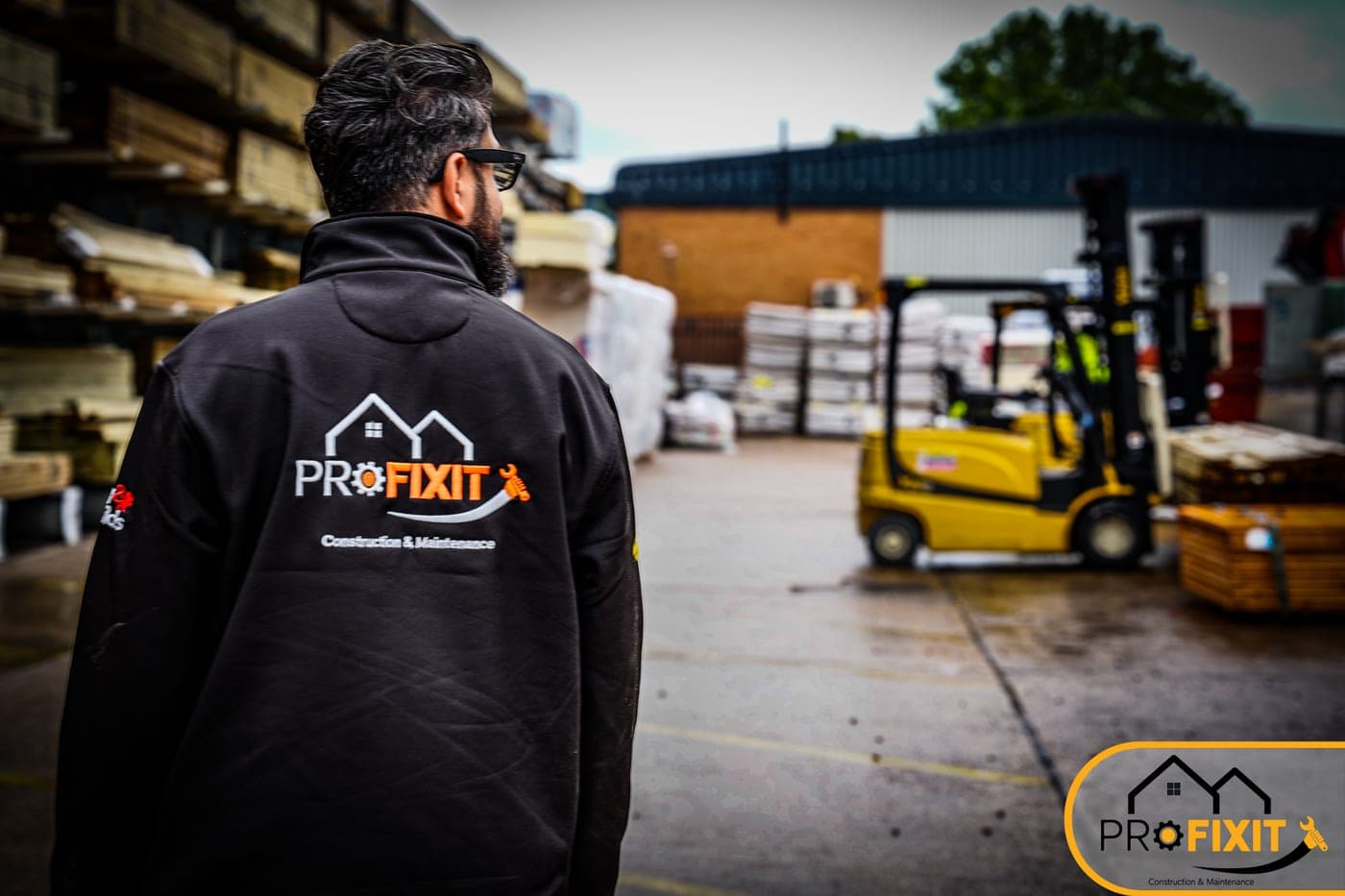 A Pro Fixit worker in a branded jacket standing in an outdoor trade yard.